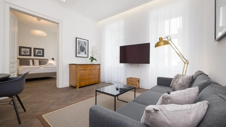 Helles Wohnzimmer mit modernem Sofa, Fischgrätparkett und Blick in ein angrenzendes Schlafzimmer.