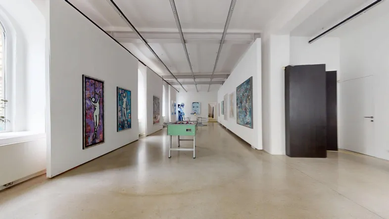 Geräumiger, heller Ausstellungsraum mit Kunstwerken an den Wänden und einem Tischfußballspiel in der Mitte.