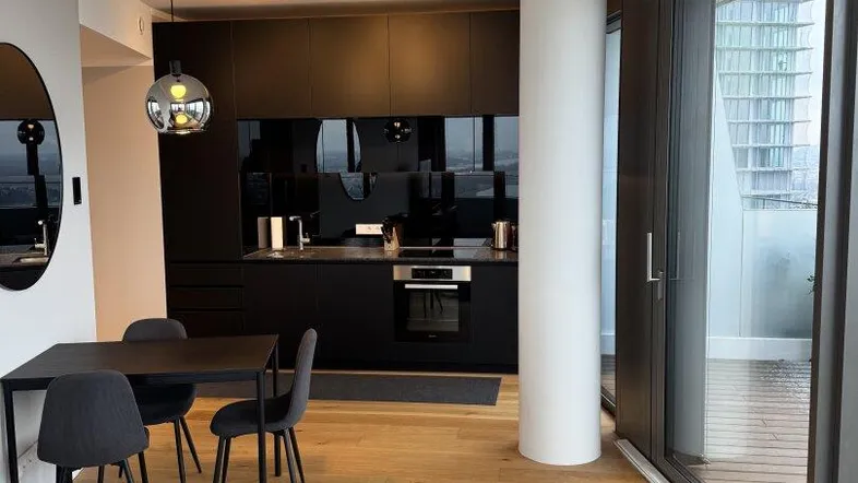 Moderne offene Wohnküche mit dunklen Schränken, Holzboden und Zugang zum Balkon.
