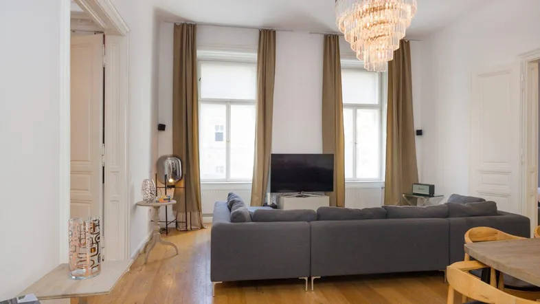 Helles Wohn- und Esszimmer mit Parkettboden, großem Sofa und elegantem Kronleuchter.