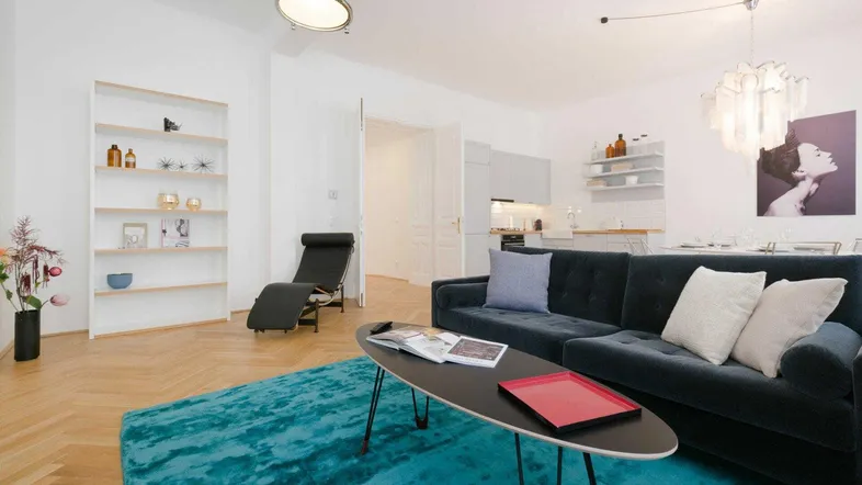 Helles Wohnzimmer mit modernem Sofa, Teppich und offener Küchenzeile, ideal für geselliges Beisammensein.