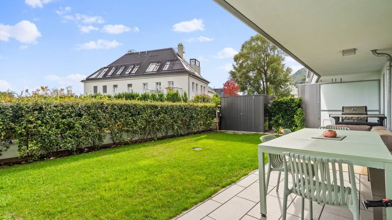Gepflegter Gartenbereich mit Rasenfläche, Hecke und Sitzgelegenheiten im Freien.