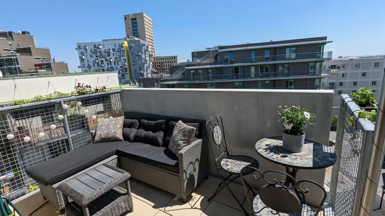 Möblierter Balkon mit Sitzgelegenheiten und Blick auf die umliegende Stadtlandschaft.