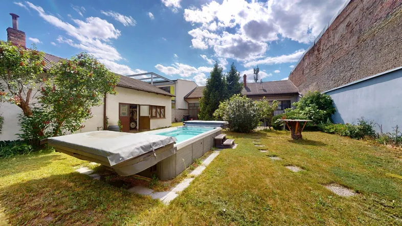Großer Gartenbereich mit integriertem Whirlpool und Rasenfläche, umgeben von Gebäuden und einer alten Mauer.