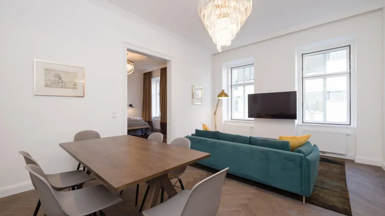 Heller Wohn- und Essbereich mit modernem Esstisch, bequemer Couch und elegantem Kronleuchter.