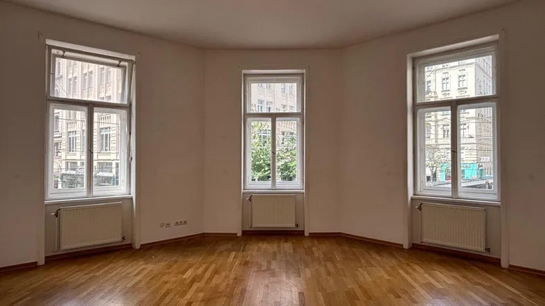 Helles Zimmer mit Parkettboden und drei großen Fenstern, die viel Tageslicht hereinlassen.