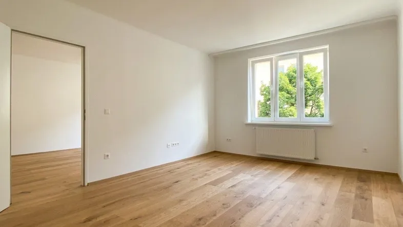Helles Zimmer mit neuem Holzfußboden und Blick ins Grüne, ideal als Wohn- oder Schlafzimmer.