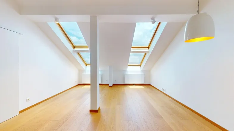 Helles Dachgeschosszimmer mit Holzboden und mehreren Dachfenstern, das viel Tageslicht hereinlässt.