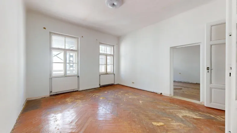 Geräumiges Zimmer mit altem Fischgrätparkett und hellen Fenstern, bereit zur Renovierung.