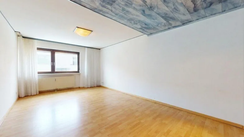 Helles Zimmer mit Holzparkettboden und einem Fenster, das viel Tageslicht hereinlässt.
