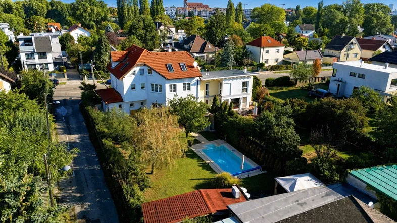 Luftaufnahme eines Hauses mit Garten, Pool und umliegender Wohngegend unter blauem Himmel.