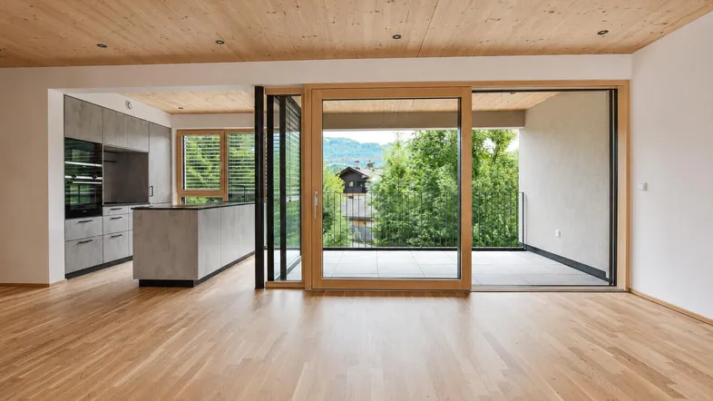 Heller offener Wohnbereich mit Holzboden, moderner Küche und Zugang zu einem Balkon mit Bergblick.