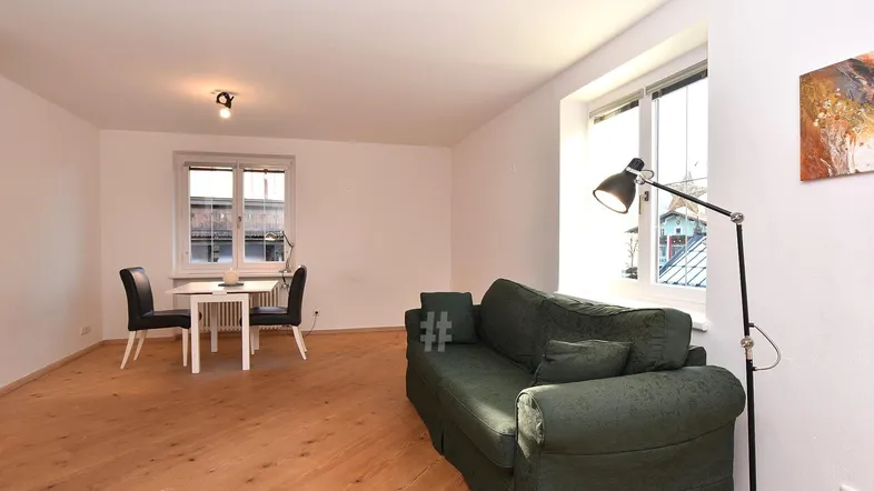 Helles Wohnzimmer mit Holzboden, einem grünen Sofa und einem kleinen Essbereich am Fenster.
