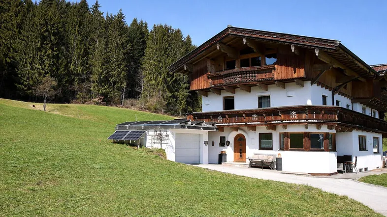 Traditionelles Haus im alpinen Stil mit Holzbalkonen, umgeben von grünen Wiesen und Wald.
