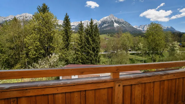 Panoramablick vom Holzbalkon auf die majestätischen Berge und die umliegende grüne Landschaft.