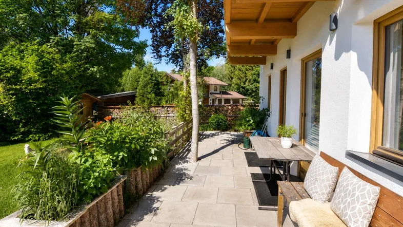 Sonniger Terrassenbereich mit Holzbänken und üppiger Bepflanzung, ideal zum Entspannen im Freien.