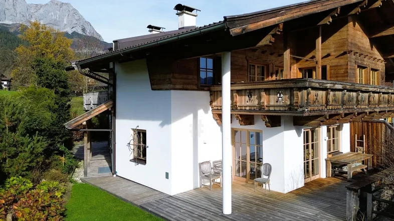 Traditionelles Holzchalet mit weißer Fassade, großer Holzterrasse und beeindruckendem Bergblick.