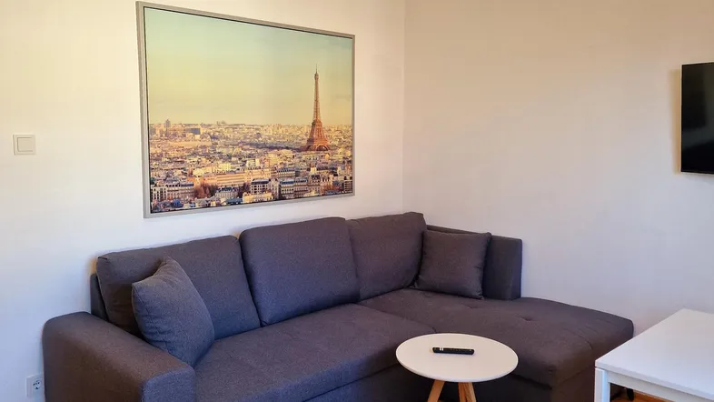 Gemütliches Wohnzimmer mit Ecksofa, Holzboden und einem Bild der Pariser Skyline.