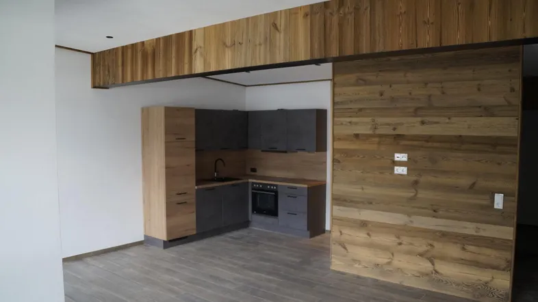 Moderne Küche mit grauen Schränken, dunkler Arbeitsplatte und rustikalen Holzverkleidungen an Wänden und Decke.