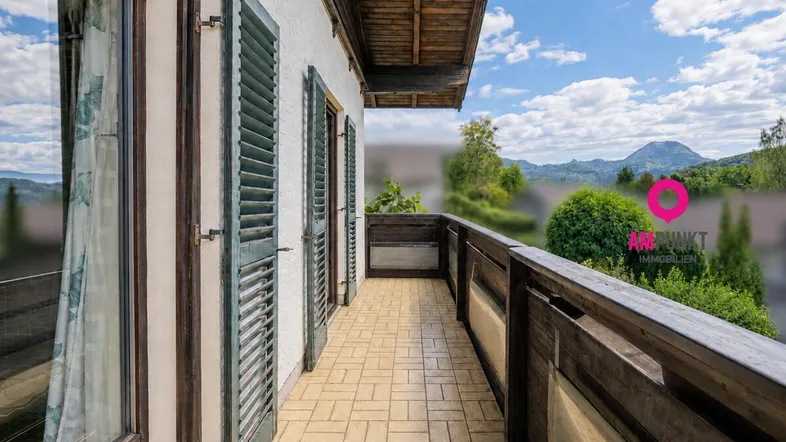 Langer Balkon mit Holzboden und grünen Fensterläden, bietet einen weiten Blick auf die Landschaft.