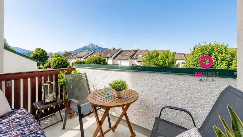Gemütlicher Balkon mit Holzboden, Sitzgelegenheiten und weitem Bergblick unter blauem Himmel.
