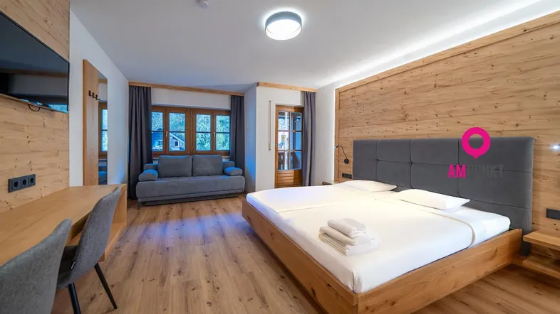Geräumiges Schlafzimmer mit Holzboden, Doppelbett, Sofa und Schreibtischbereich, hell und modern eingerichtet.