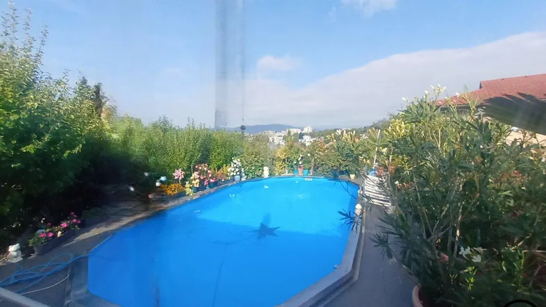 Großer Außenpool im Garten mit blauer Abdeckung und weitem Blick auf die Umgebung.