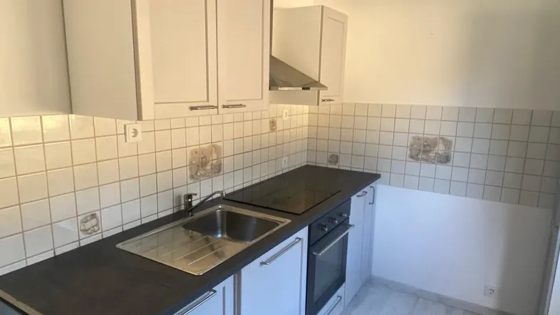 Kleine Küche mit hellen Schränken, dunkler Arbeitsplatte und Fliesenrückwand, ausgestattet mit Ofen und Kochfeld.