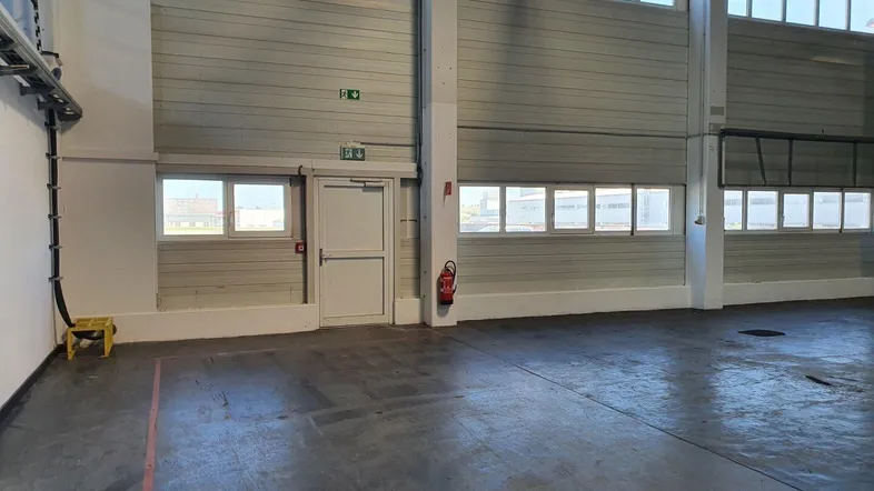 Große, leere Lagerhalle mit hohen Decken, vielen Fenstern und einem robusten Betonboden.