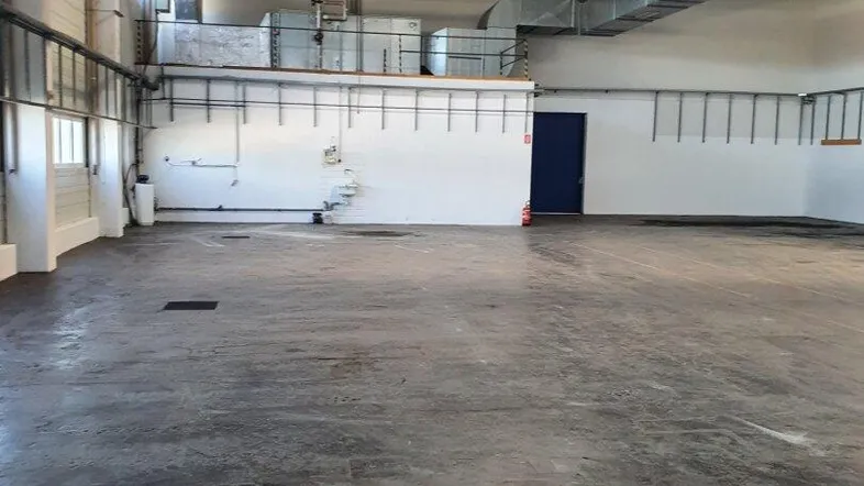 Geräumige Lagerhalle mit hohen Decken, Betonboden und sichtbaren Lüftungsrohren, ideal für industrielle Nutzung.