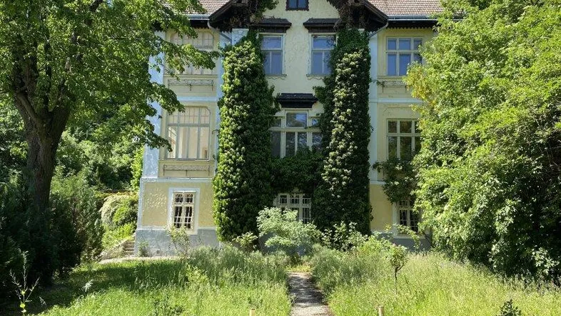 Prächtige historische Villa mit gepflegtem Vorgarten und üppiger Vegetation an einem sonnigen Tag.
