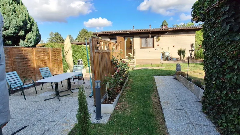 Rückansicht des Hauses mit gepflasterter Terrasse, Gartenmöbeln und umgebender Hecke.