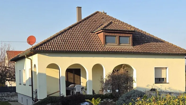 Einfamilienhaus mit gelber Fassade, Satteldach und Gaubenfenstern unter blauem Himmel.