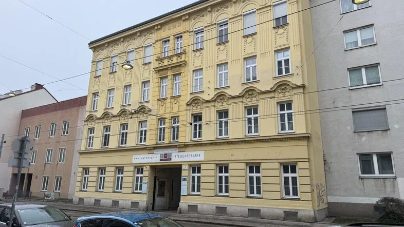 Historische Fassade eines Mehrfamilienhauses in Gelb mit vielen Fenstern und Straßenblick.
