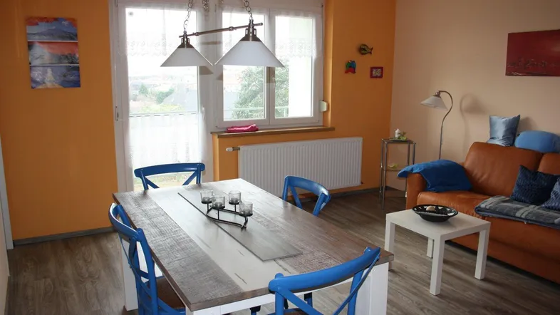 Heller Wohn-Essbereich mit Holztisch, blauen Stühlen und Zugang zum Balkon, ideal für gesellige Stunden.