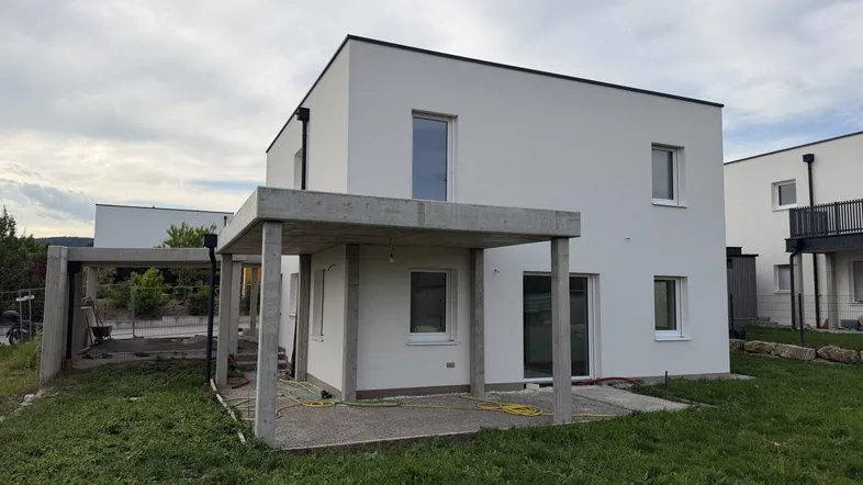 Modernes Einfamilienhaus im Bau mit weißer Fassade und vorbereiteter Terrasse.