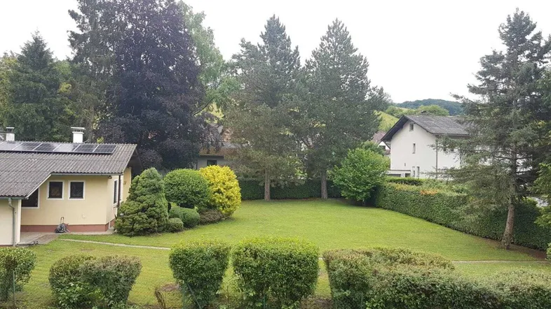 Großer Gartenbereich mit gepflegtem Rasen, Bäumen und Sitzbänken, umgeben von Hecken.