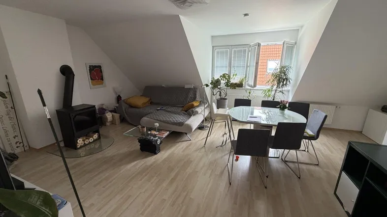 Helles Dachgeschoss-Wohnzimmer mit Kaminofen, Esstisch und schrägen Wänden.
