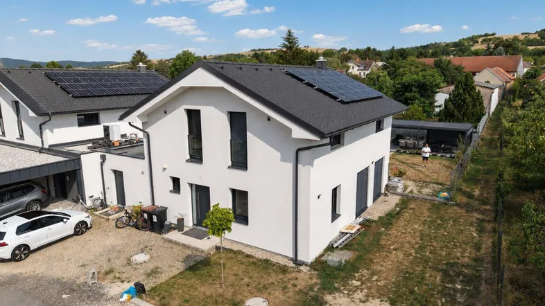 Modernes Einfamilienhaus mit Photovoltaikanlage und gepflegtem Vorgarten unter blauem Himmel.