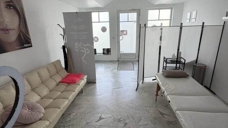 Heller Gewerberaum mit beigem Sofa, Massageliege und großen Fenstern, ideal für ein Studio.