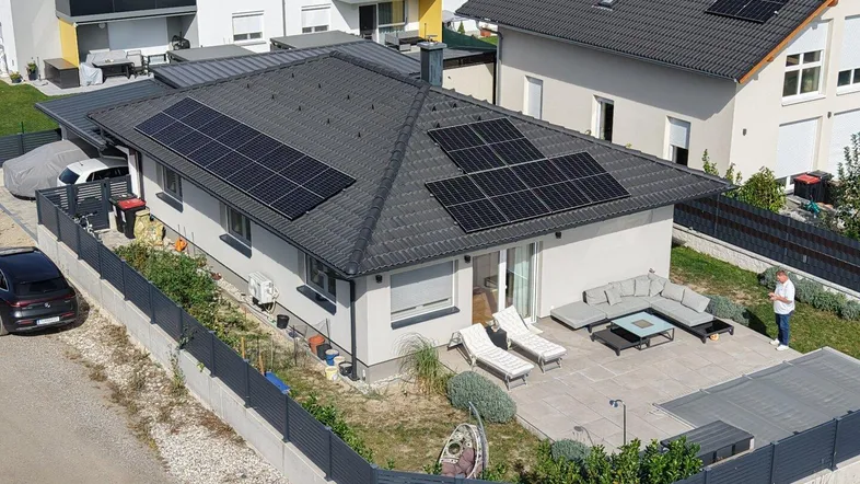 Vogelperspektive eines Einfamilienhauses mit großer möblierter Terrasse, Garten und Solaranlage auf dem Dach.