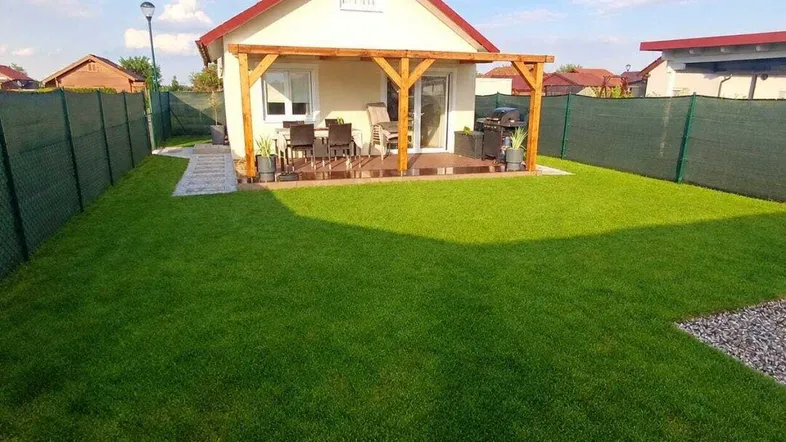 Gepflegter Garten mit Rasenfläche und einer möblierten Terrasse unter einer Holzpergola.