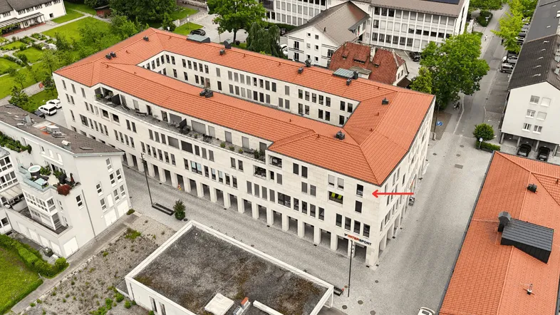Luftaufnahme eines modernen Gebäudekomplexes mit rotem Ziegeldach und umliegender Stadtlandschaft.