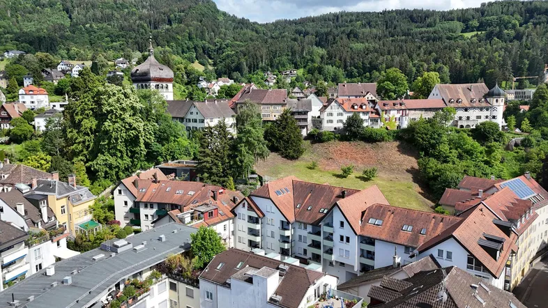 Panoramablick auf eine malerische Stadt mit traditionellen Häusern und grünen Hügeln im Hintergrund.