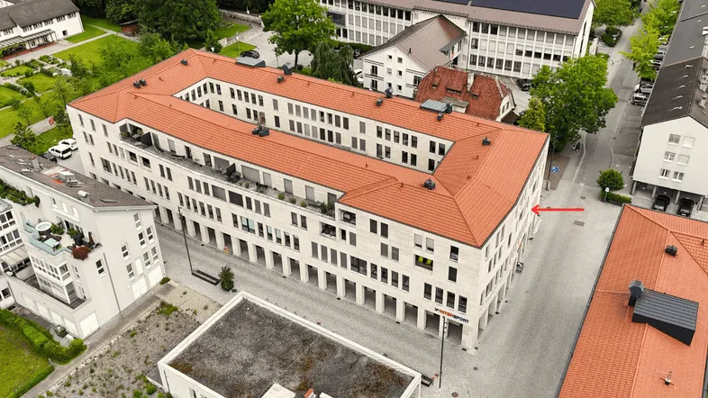 Luftaufnahme eines modernen Gebäudekomplexes mit rotem Ziegeldach und umliegender Stadtlandschaft.