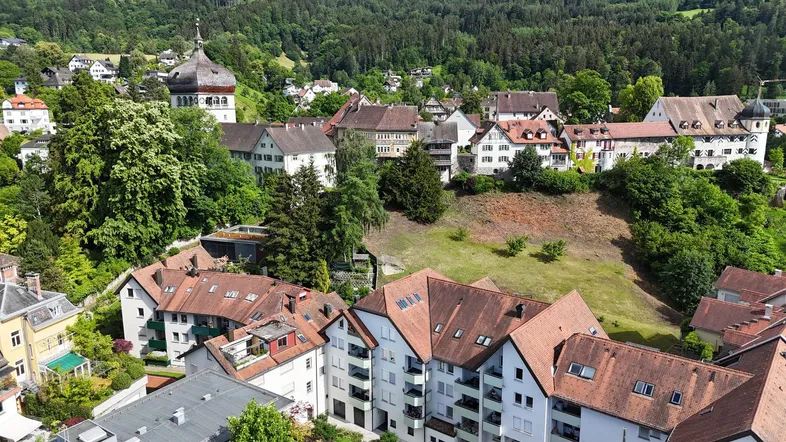 Luftaufnahme einer malerischen Stadt mit traditionellen Häusern und grünen Hügeln im Hintergrund.