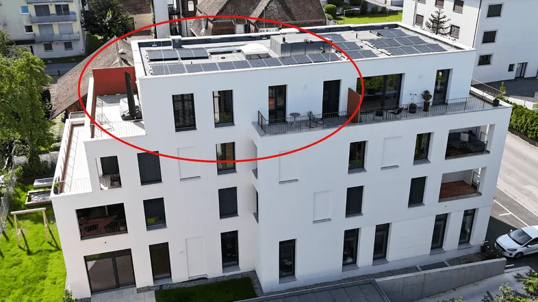 Luftaufnahme eines modernen Wohngebäudes mit Flachdach und Solaranlagen in einer städtischen Umgebung.