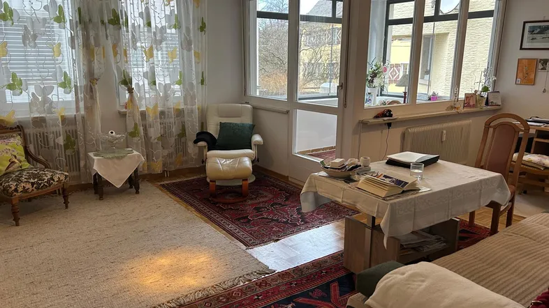 Gemütliches Wohnzimmer mit Teppichen, bequemen Möbeln und Zugang zu einem verglasten Balkon.