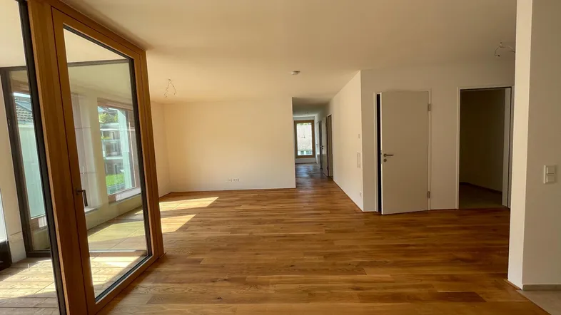 Helles, leeres Wohnzimmer mit neuem Parkettboden und Zugang zu einem Balkon.
