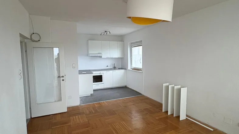 Helles Zimmer mit Parkettboden und integrierter Küchenzeile in einem offenen Wohnbereich.